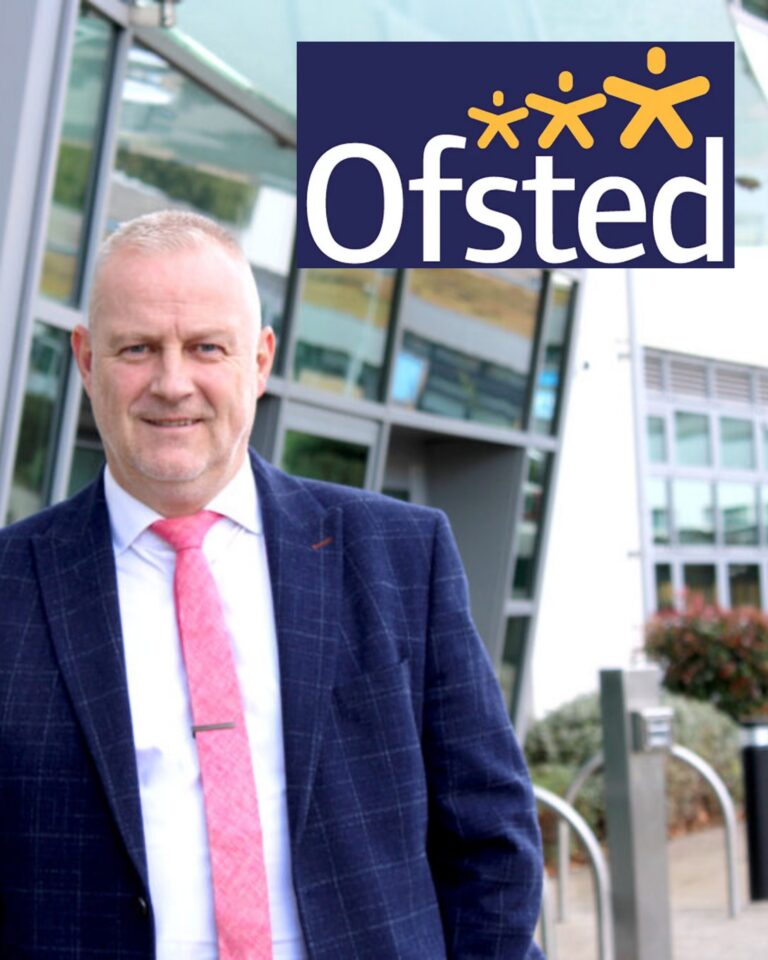 A professionally dressed person in a suit and pink tie standing outside a modern school building, with the Ofsted logo displayed in the top corner of the image.